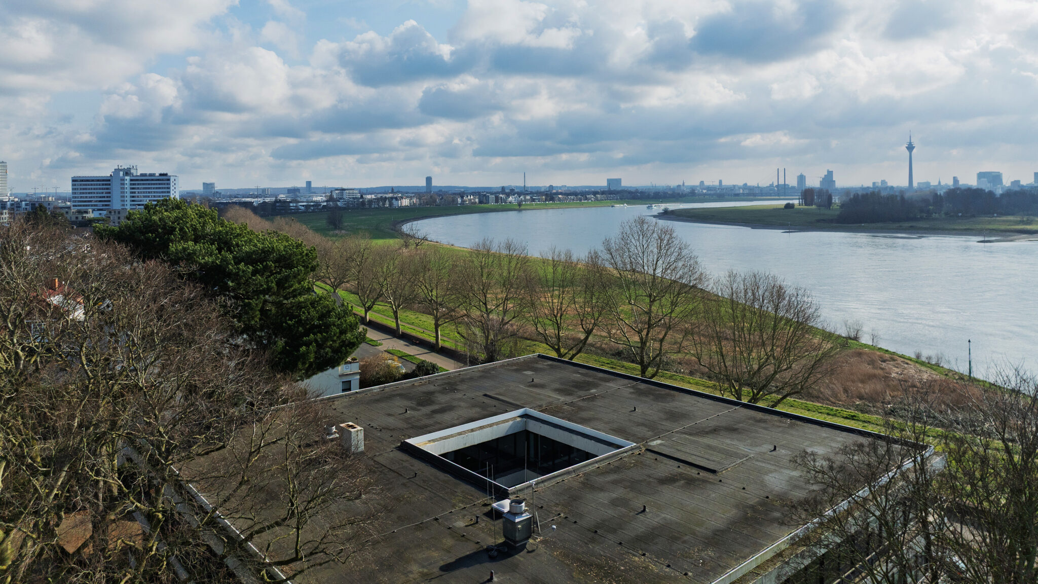 Luftbild, im Vordergrund das Dach des Gebäudes, im Hintergrund ein Fluss und eine Stadt